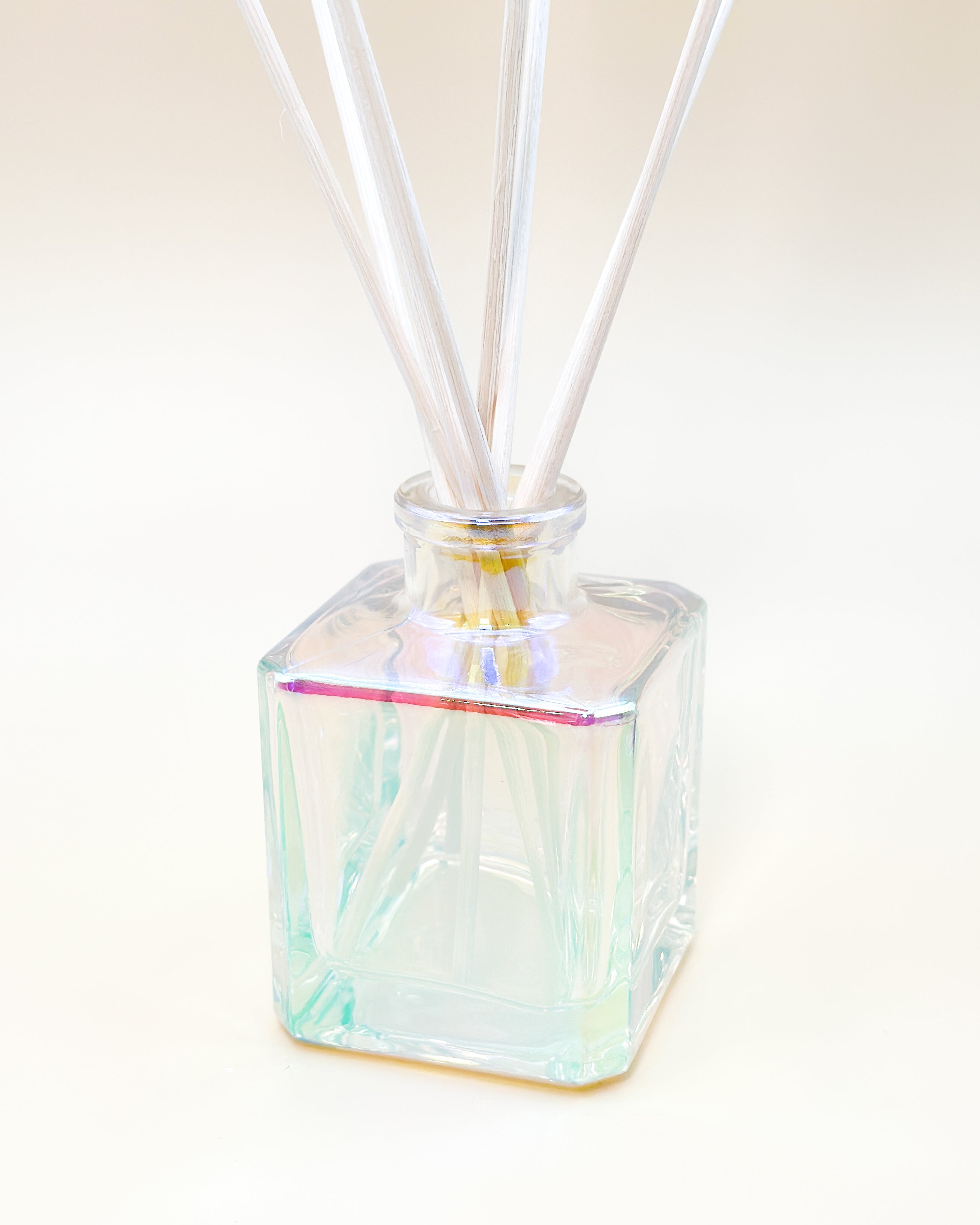 Iridescent glass diffuser with white sticks on a light beige background