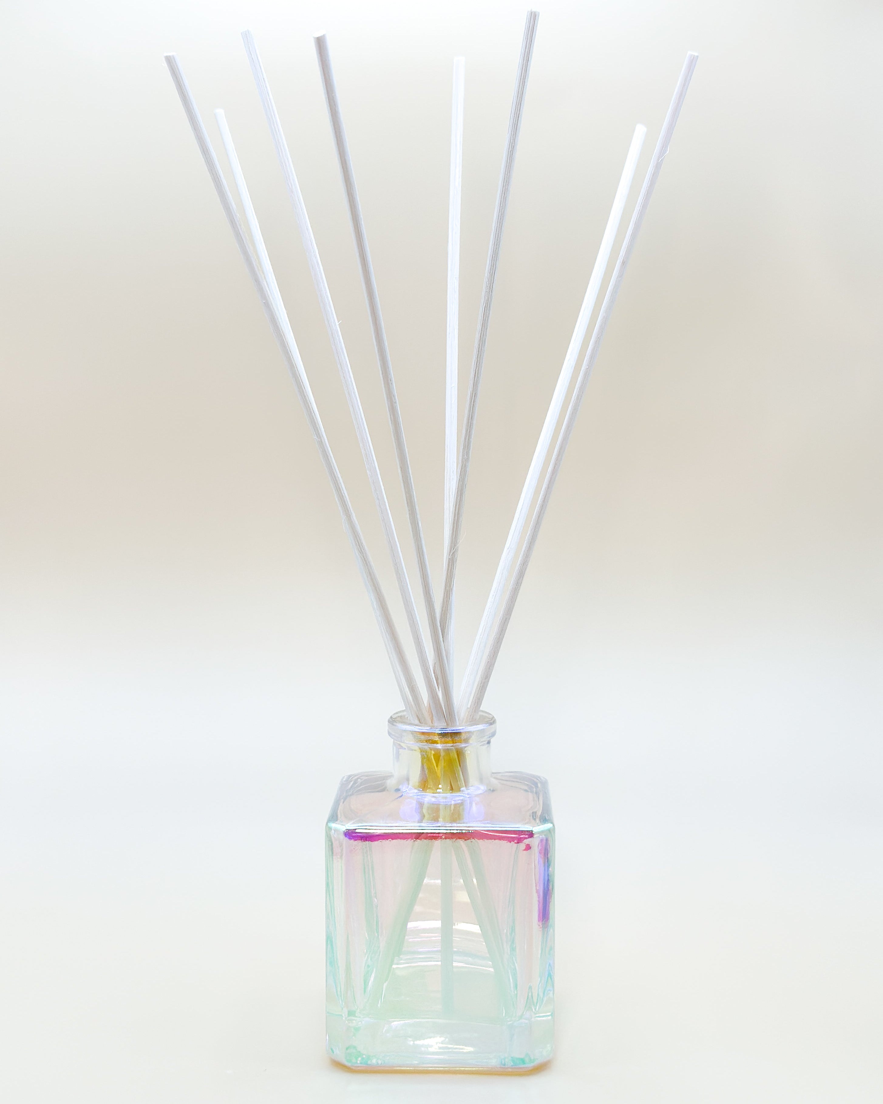 Reed diffuser with white sticks in a clear iridescent bottle on a light background