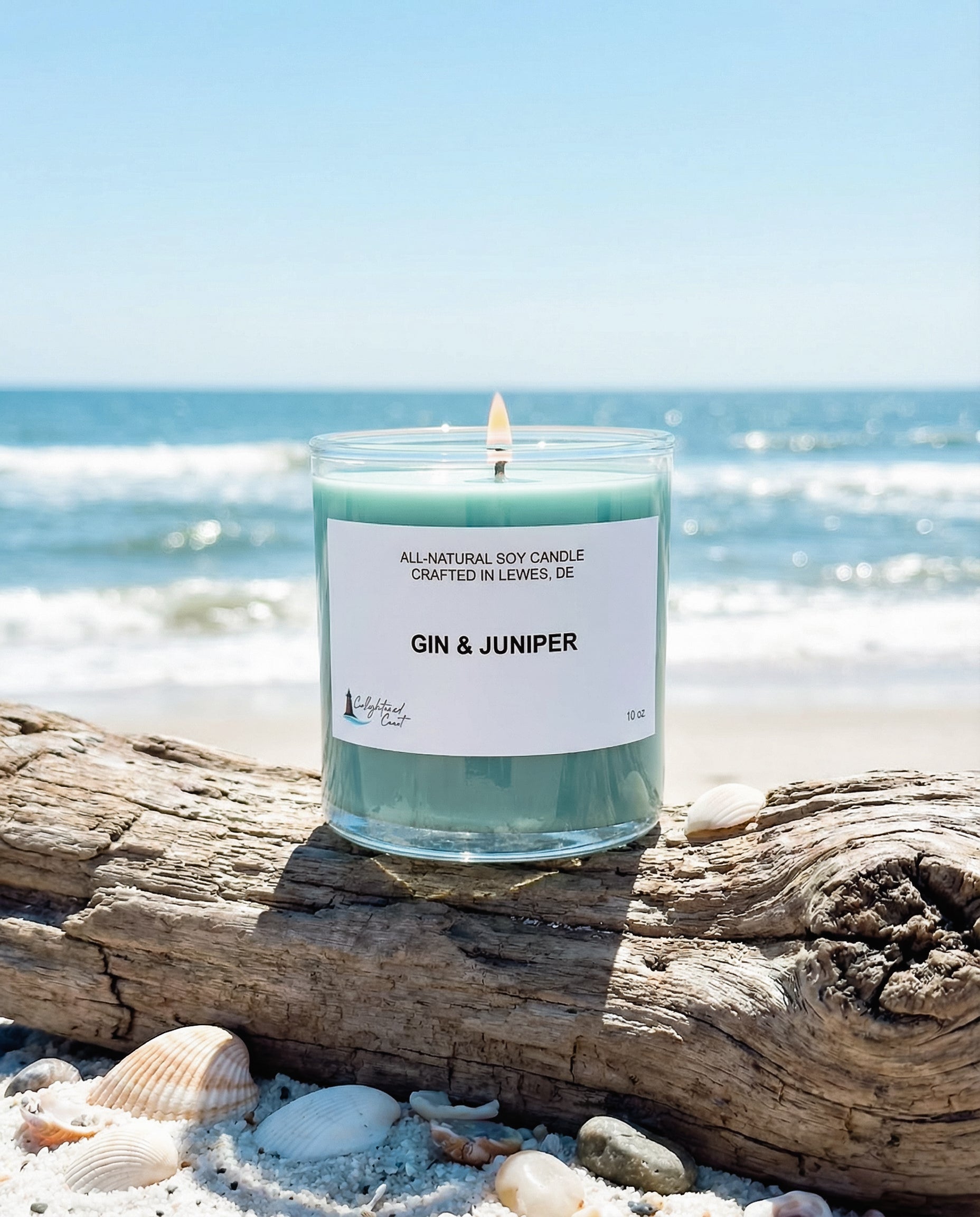 Candle labeled 'Gin & Juniper' on a beach with ocean in the background