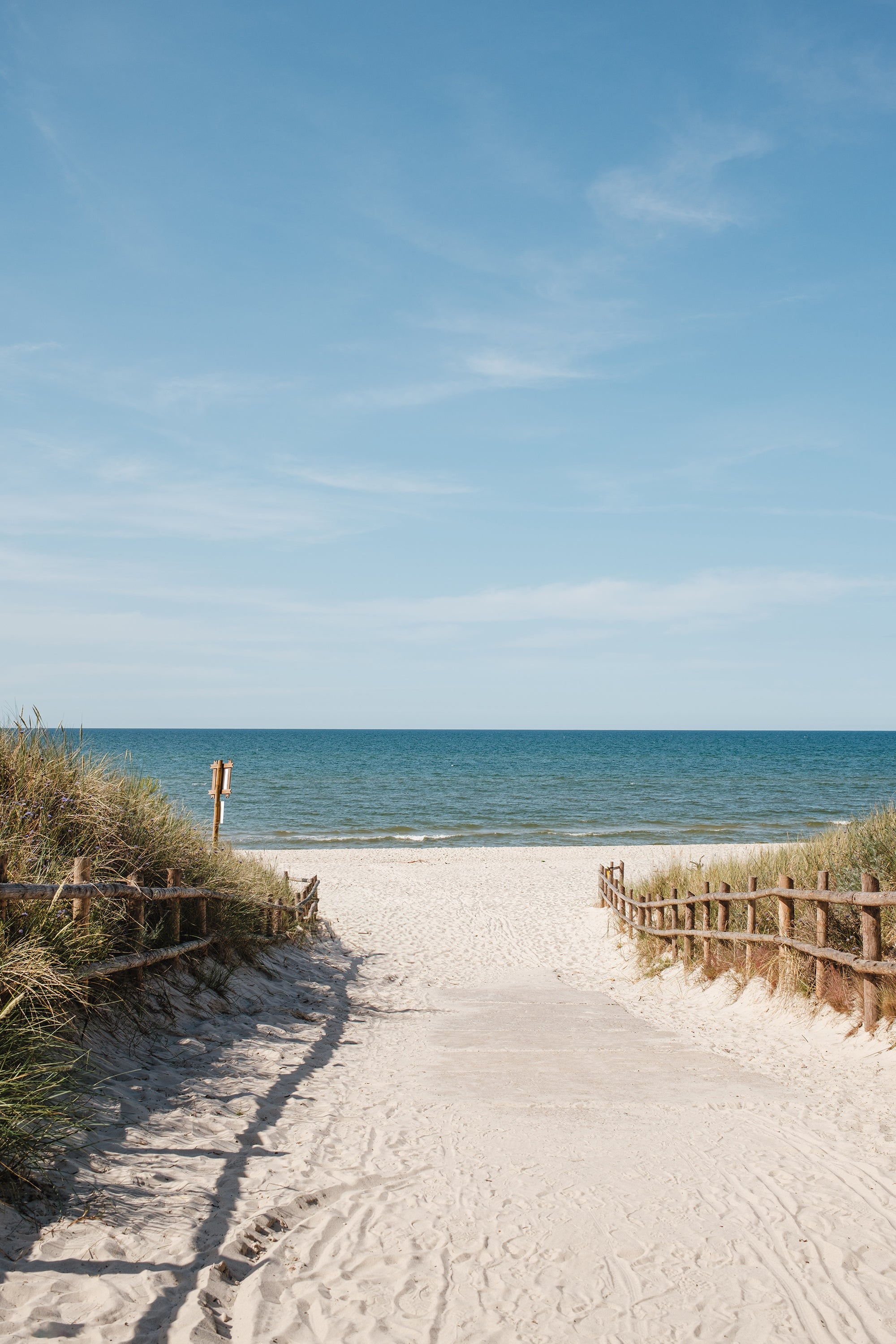 Beach scene with a wooden path leading to the ocean under a clear blue sky.