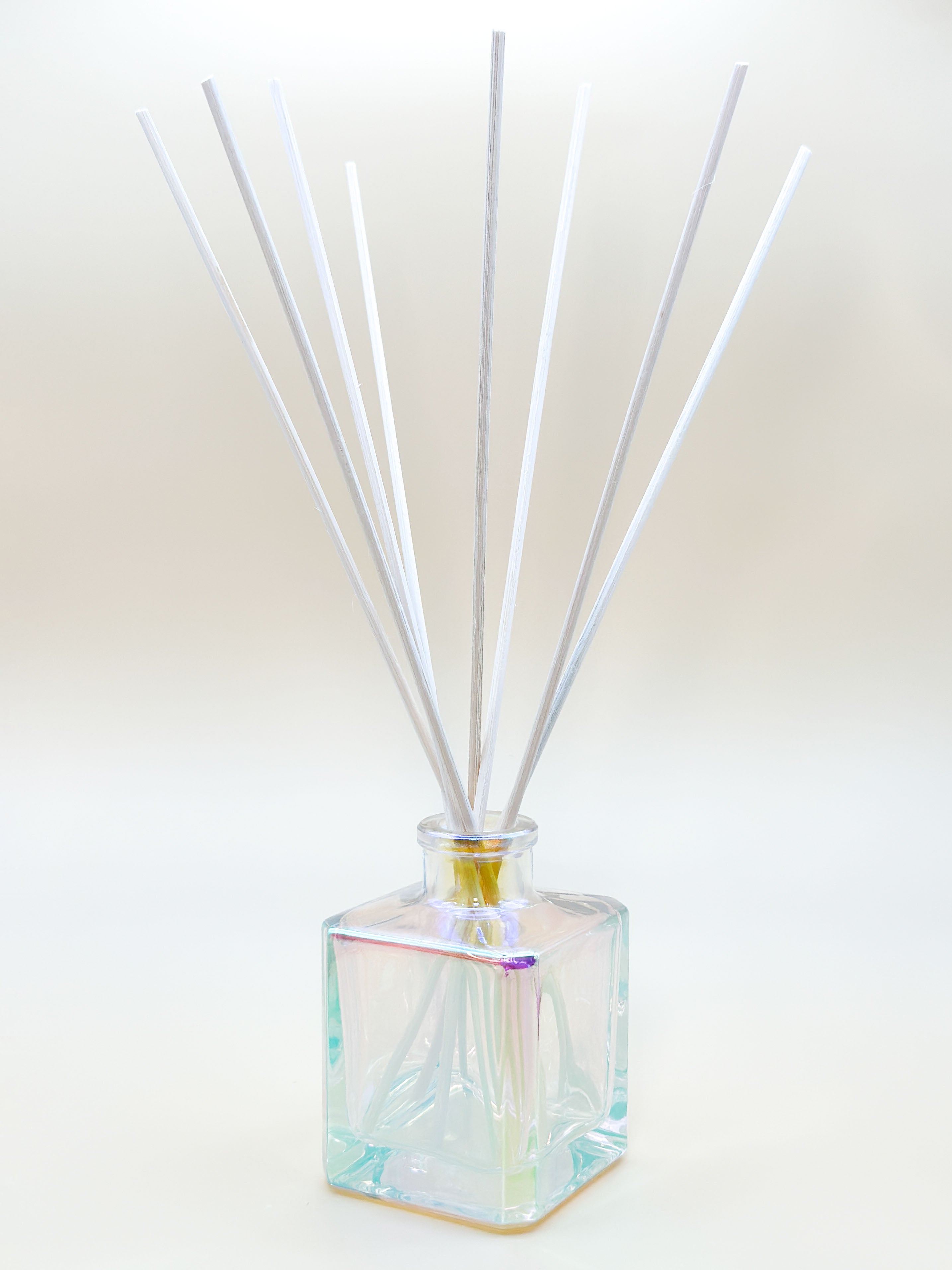 Iridescent diffuser bottle with white reeds on a light background